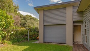 A residential building with a garage door, a wooden deck, and a grassy yard. - Cooks Getaway - Cooks Beach Holiday Home (Cooks Beach)