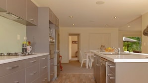 A modern kitchen with grey cabinets, a central island, and a wooden floor. - Cooks Getaway - Cooks Beach Holiday Home (Cooks Beach)