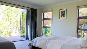 A bedroom with a bed, a window, and a door leading to an outdoor area. - Cooks Getaway - Cooks Beach Holiday Home (Cooks Beach)
