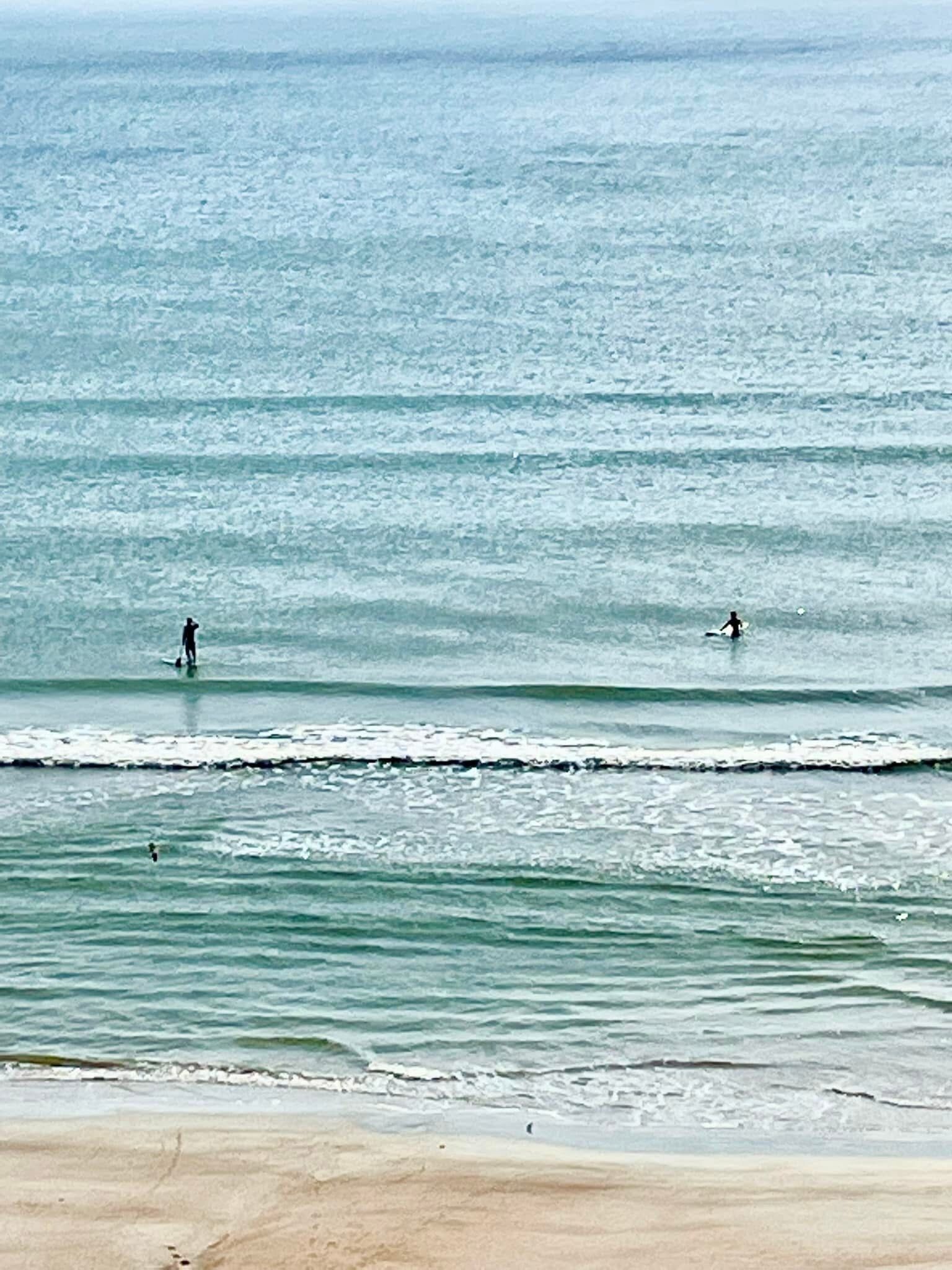 Una playa con olas y dos personas en el agua.