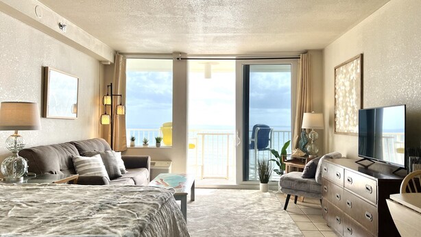 Ein geräumiges Schlafzimmer mit einem großen Bett, einem Schminktisch, einem Fernseher und einem Balkon mit Meerblick.