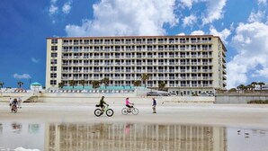 Ein großes Hotel mit mehreren Etagen und Balkonen, in Strandnähe mit spiegelnder Wasseroberfläche.