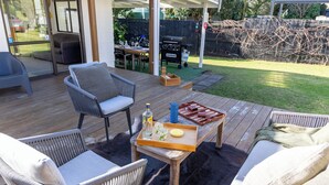 Een houten terras met rieten meubilair, een barbecue en een overdekte patio.