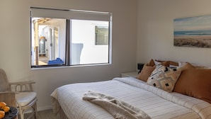 Een slaapkamer met een groot bed, een raam met uitzicht op een strand, een stoel en een tafel met sinaasappels.