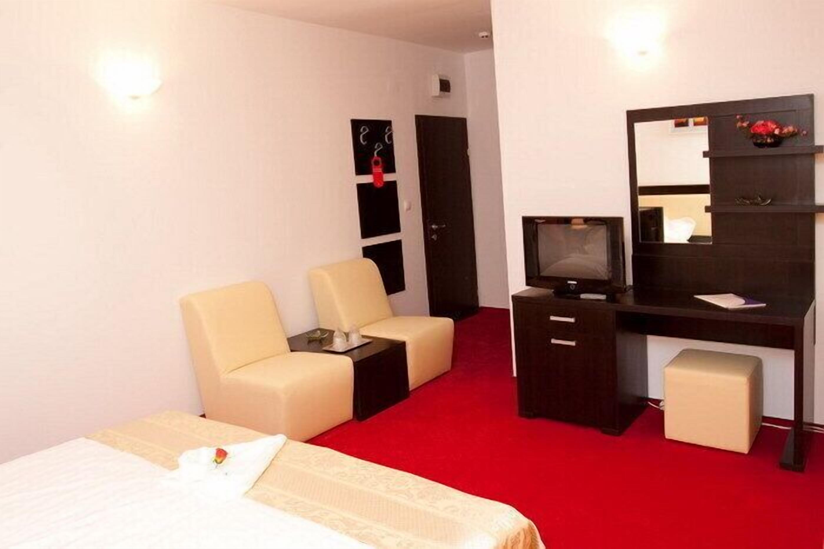 A hotel room with a bed, a desk with a computer, a chair, a small table, and a wardrobe.