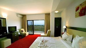 A hotel room with a large bed, a television, a desk, a chair, and a view of the outdoors. - Pensiunea SIERA (Constanta)