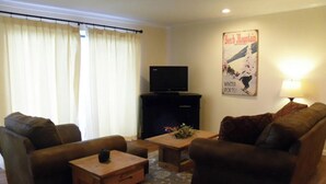 A living room with two brown leather sofas, a wooden coffee table, a flat-screen TV on a black stand, and a poster on the wall. - Extra Clean Next Beech Mountain Ski Resort (Beech Mountain)