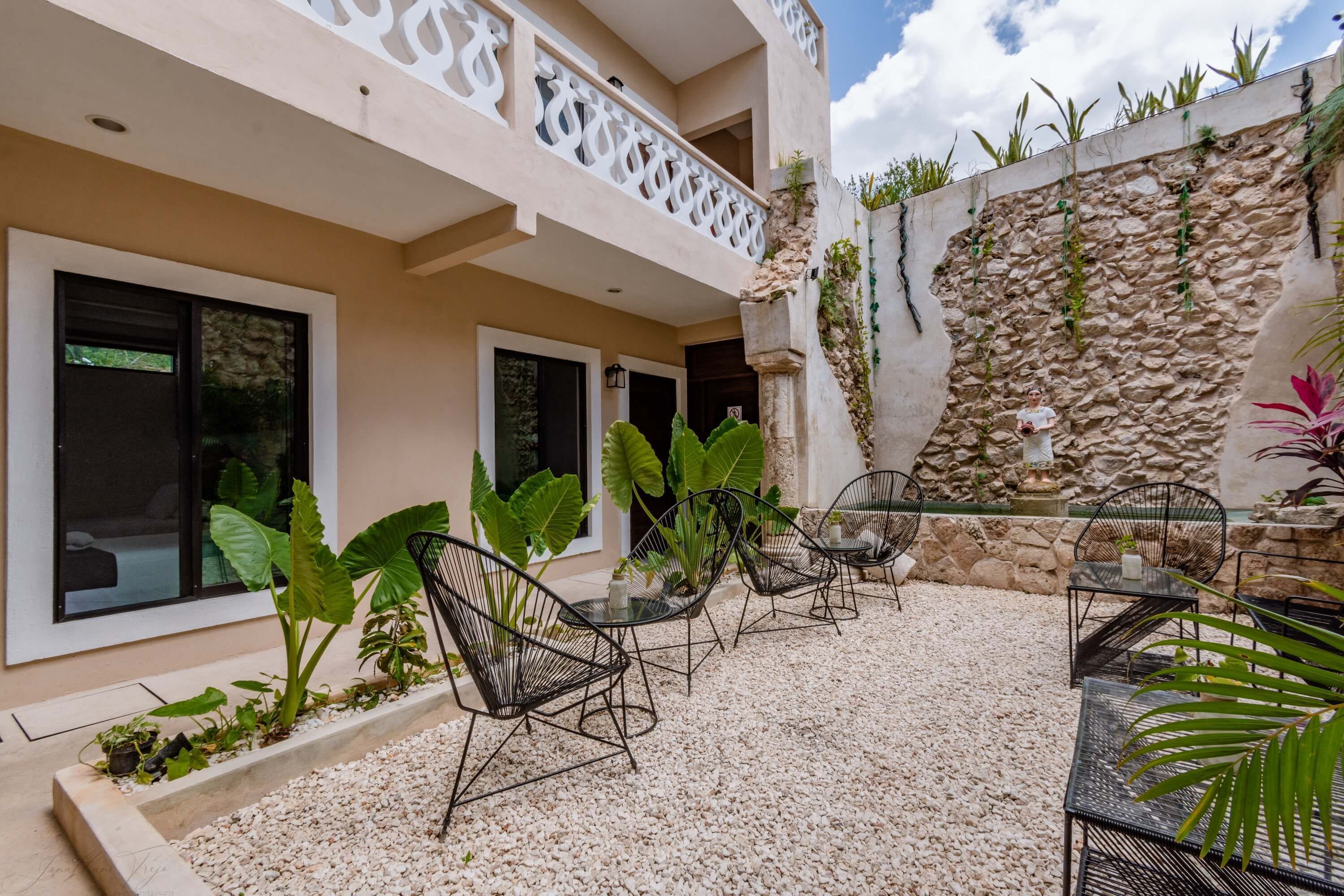 A modern outdoor seating area with chairs and tables, surrounded by a gravel floor and potted plants.