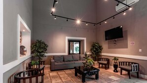 Un salon moderne avec un canapé, une table basse et des fauteuils, un téléviseur à écran plat fixé au mur et des luminaires au plafond.