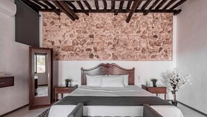 Une chambre avec un plafond imitant la pierre, un cadre de lit en bois, un banc au pied du lit et une table de chevet agrémentée d’une plante.