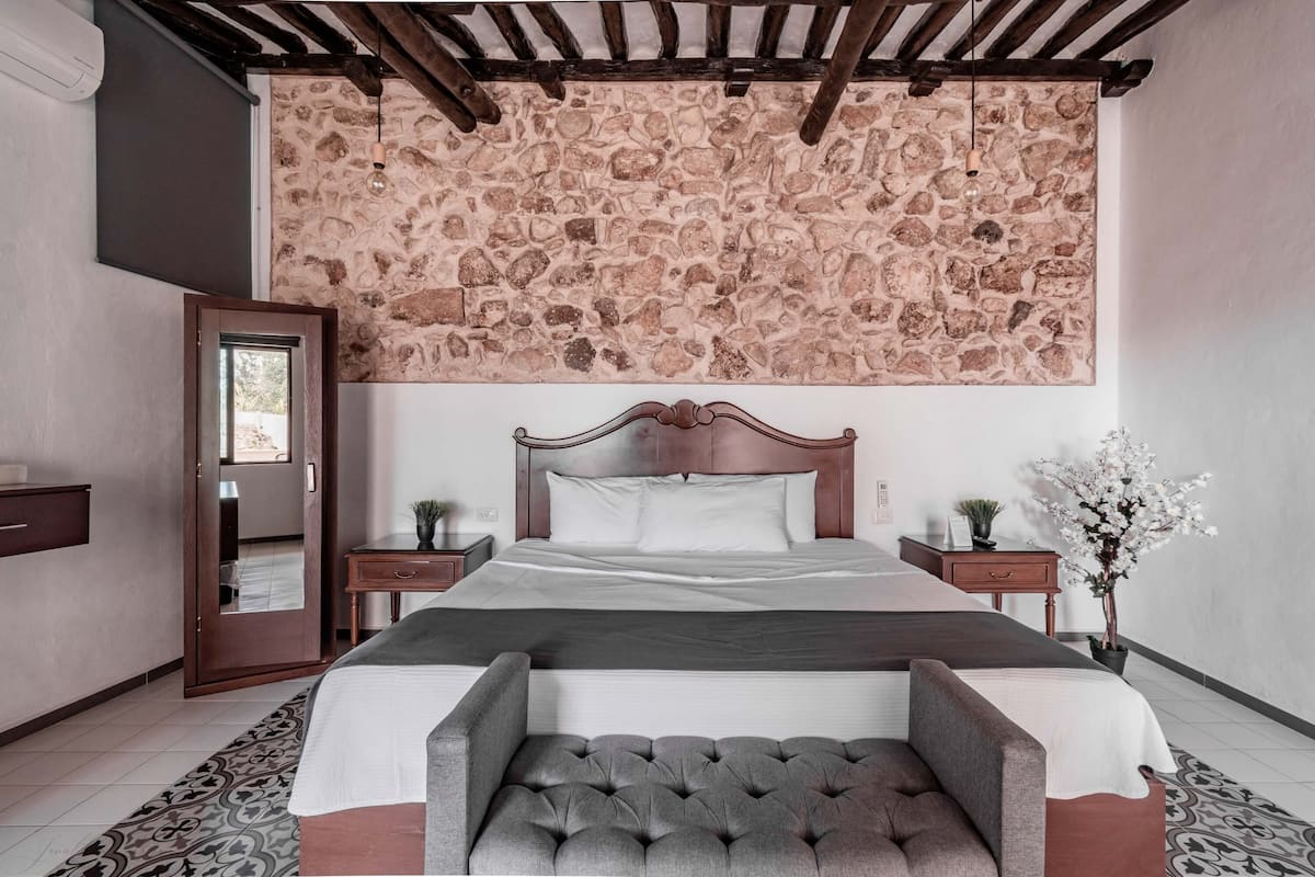 A bedroom with a stone-patterned ceiling, a wooden bed frame, a bench at the foot of the bed, and a nightstand with a plant.