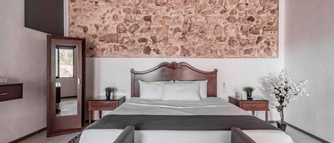 Un dormitorio con techo de diseño de piedra, estructura de cama de madera, un banco al pie de la cama y una mesita de noche con una planta.