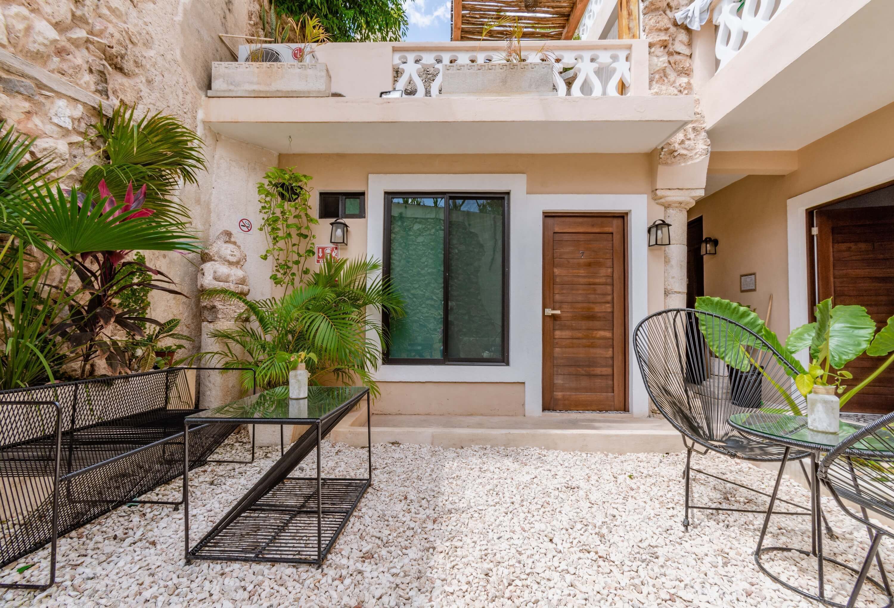 A courtyard with a seating area, a wooden door, and a balcony with plants.
