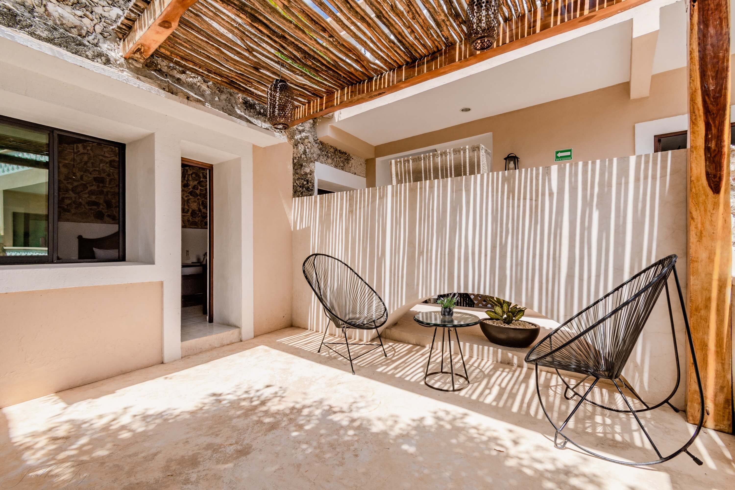 Un patio exterior moderno con dos sillas de entramado metálico, una pequeña mesa redonda y una planta en maceta.