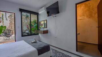 A modern hotel room with a bed, a TV mounted on the wall, a large window with a view of greenery, and a sliding door.