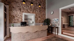 Un hall d’accueil d’hôtel avec un mur en pierre, un comptoir d’accueil, une horloge et un escalier menant à une autre partie de l’hôtel.