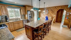 A kitchen with wooden cabinets, granite countertops, and a central island with bar stools. - Summer Slope | 130 ft from the beach | Private Pool (Virginia Beach)