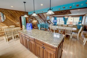Una cocina amplia con isla de granito, armarios de madera e iluminación colgante.