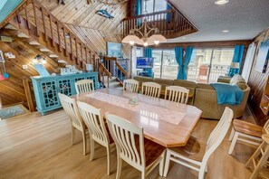 Amplia sala de estar con una escalera de madera, una mesa de comedor con sillas, un sofá y un televisor.
