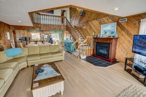 Amplia sala de estar con interior de madera, chimenea, comedor y escalera que conduce a un nivel superior.
