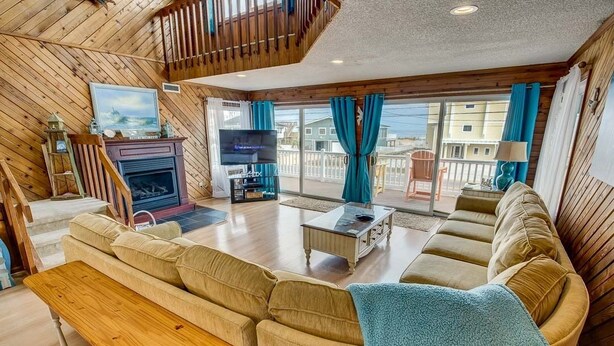 A spacious living room with a wooden interior, a fireplace, a television, and a balcony with blue curtains. - Summer Slope | 130 ft from the beach | Private Pool (Virginia Beach)