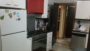 A compact kitchen with white cabinets, a red upper cabinet, a stove, and a refrigerator.