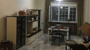 A dining area with a table and chairs, a cabinet with shelves, a window with curtains, and a chandelier.