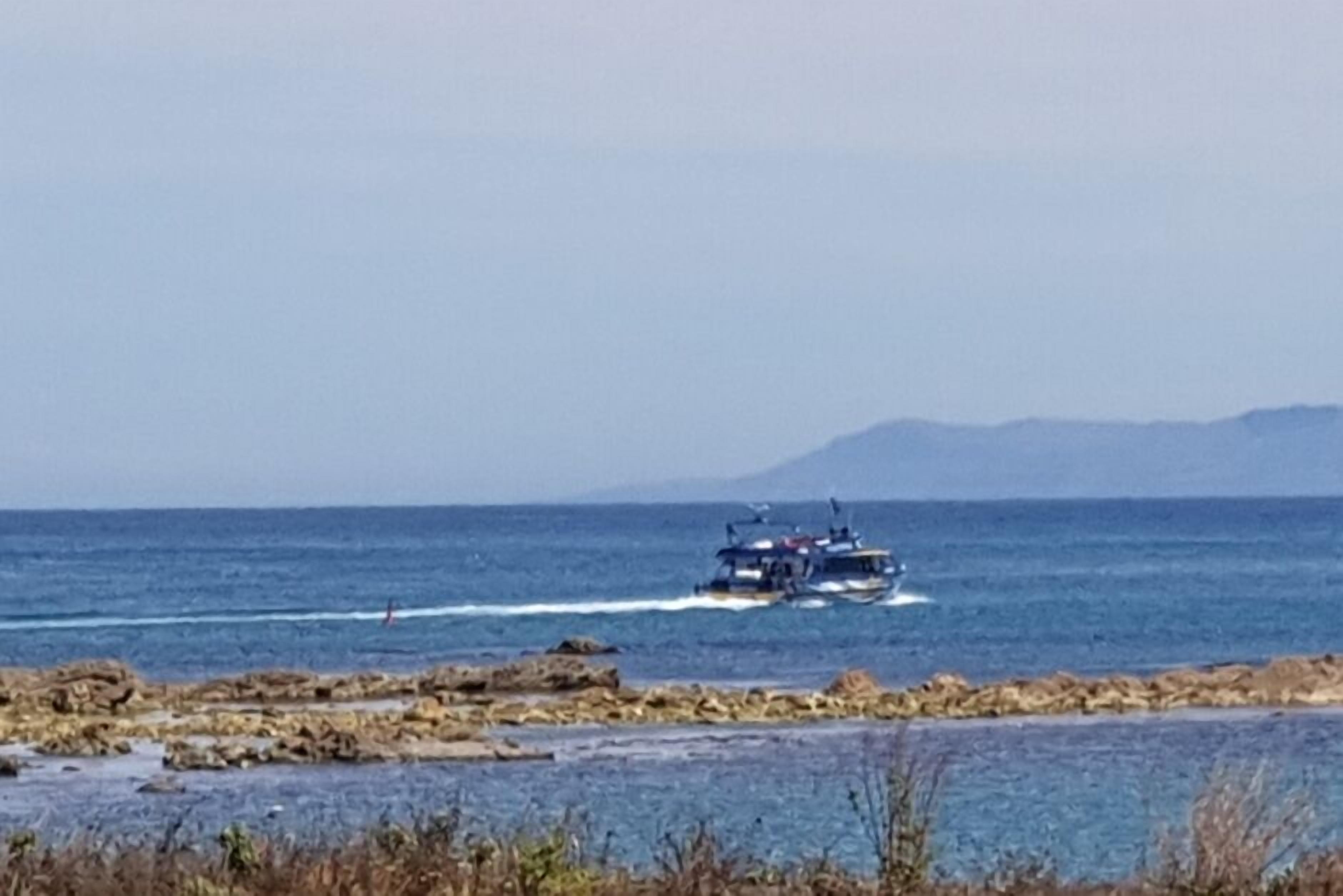 Escena costera con un bote en el agua, costa rocosa y montañas al fondo.