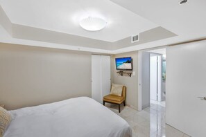 A bedroom with a bed, a chair, a television, and a door leading to another room.