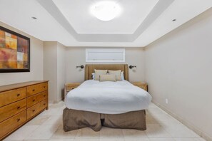 A bedroom with a bed, a wooden dresser, a ceiling light, and a wall-mounted air conditioning unit.