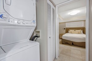 A laundry area with a washing machine and dryer, a bedroom with a bed and nightstand, and a door leading to another room.