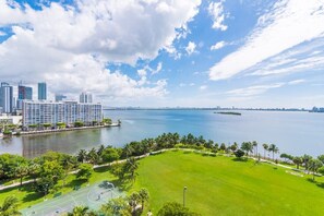 A waterfront property with a tennis court, a grassy area, and high-rise buildings in the background.