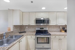 A kitchen with a stainless steel microwave, double oven, granite countertop, and white cabinetry.