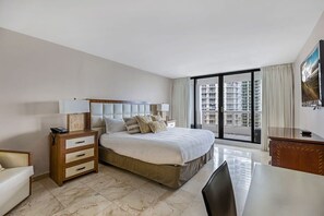 A hotel room with a bed, bedside table, desk, and a large window with a city view.
