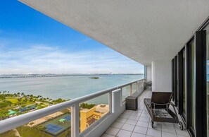 A balcony with a view of a body of water, a distant bridge, and a tennis court.