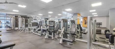 Un gimnasio con diversas máquinas de ejercicio, espejos y un ambiente limpio y bien iluminado.