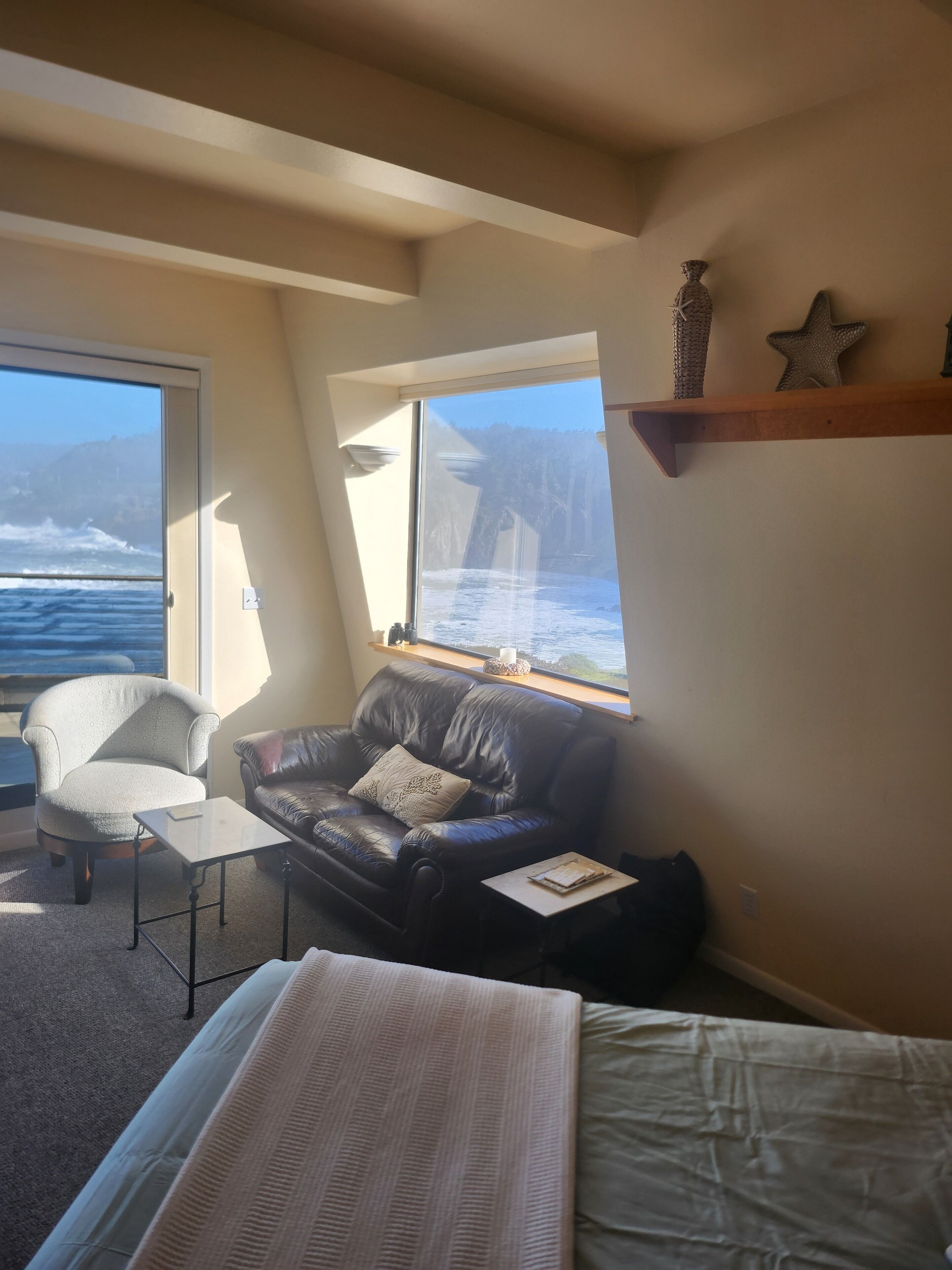 A room with a bed, a leather sofa, a chair, and a window overlooking the ocean.