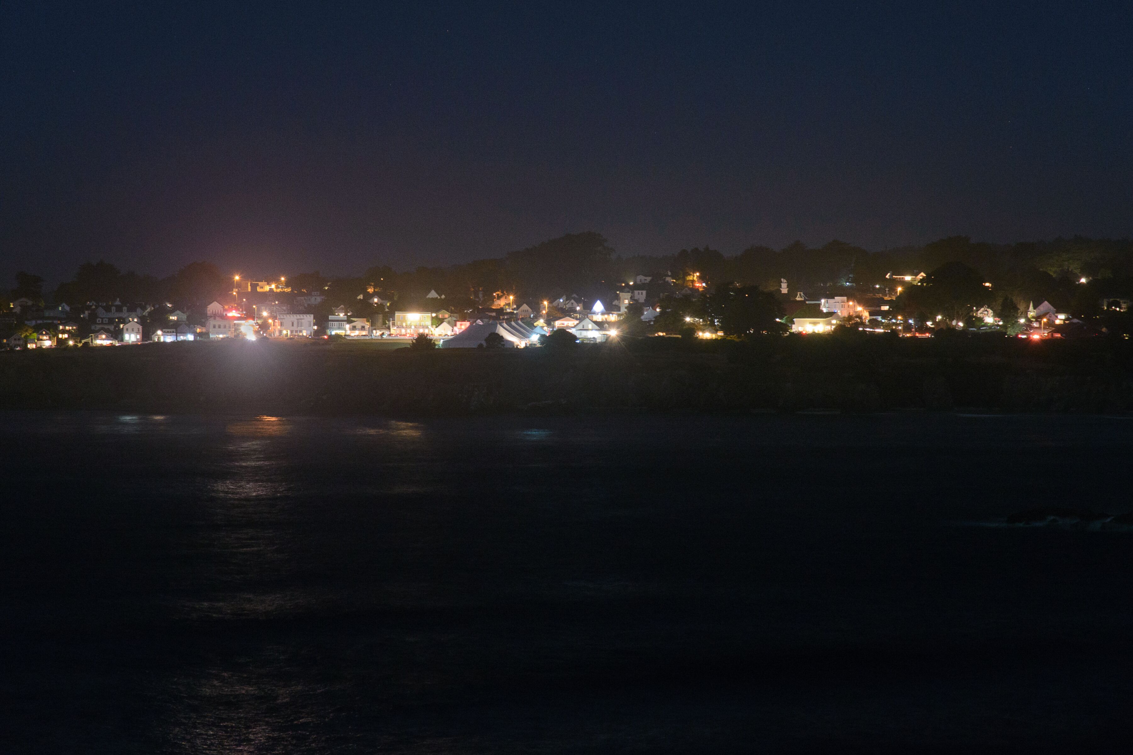 A nighttime view of a coastal town with illuminated buildings and a calm sea.
