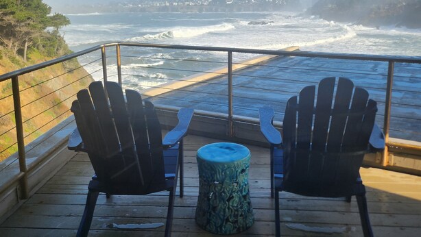 A deck with two Adirondack chairs and a small round table, overlooking a rocky coastline with waves crashing against the shore. - SWEEPING OCEAN VIEWS - bar none. Over 365 5 star reviews, everyone comes back.  (Mendocino)