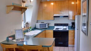 A compact kitchen with wooden cabinets, a microwave, a stove, and a refrigerator. There is a dining table with chairs and a small shelf with decorative items. - SWEEPING OCEAN VIEWS - bar none. Over 365 5 star reviews, everyone comes back.  (Mendocino)