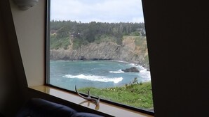 A room with a large window overlooking a coastal landscape, including cliffs and ocean waves. - SWEEPING OCEAN VIEWS - bar none. Over 365 5 star reviews, everyone comes back.  (Mendocino)