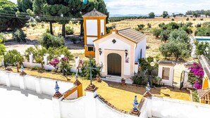Una pequeña capilla con un campanario, rodeada por un muro blanco con detalles decorativos y plantas en macetas.
