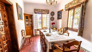 Comedor con una mesa dispuesta para cuatro comensales, sillas de madera, un candelabro y una persiana con estampado floral.
