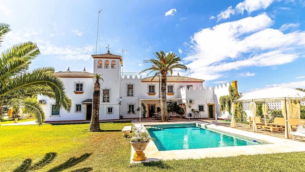 Un edificio blanco con piscina, palmeras y cielo despejado.