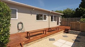 Ein Bungalow mit einer Holzterrasse, einem Gartenschlauch und einem Holzzaun.