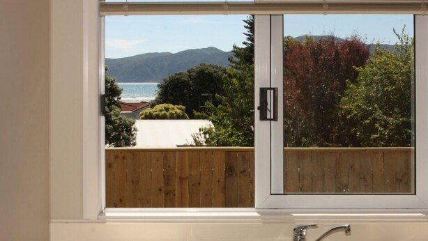 Eine Küche mit einem großen Fenster, das auf eine Holzterrasse und eine Aussicht auf das Meer und die Berge blickt.