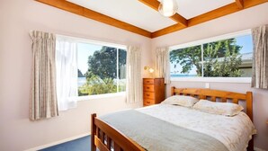 Ein Schlafzimmer mit einem hölzernen Bett, zwei Fenstern mit Vorhängen, einem Schminktisch und einer Deckenleuchte.