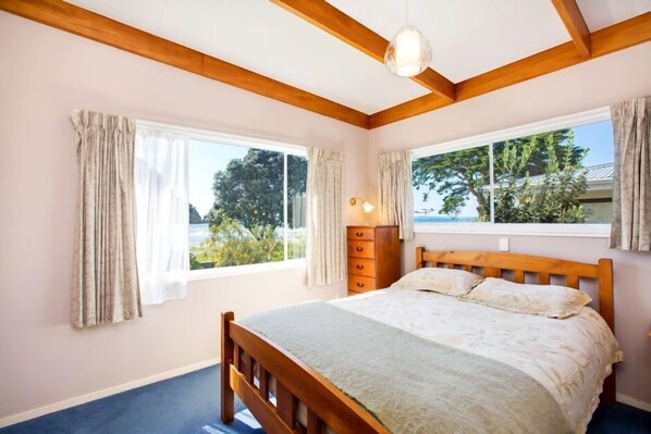 Une chambre à coucher avec un lit en bois, deux fenêtres avec des rideaux, une commode et un luminaire au plafond.