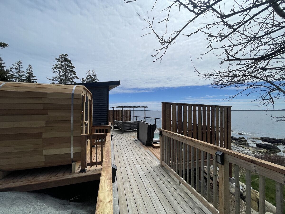 A wooden deck with a view of the water, a wooden building, and a bench.