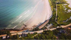 Vista aérea de una zona costera con playa, carretera y un pequeño asentamiento.